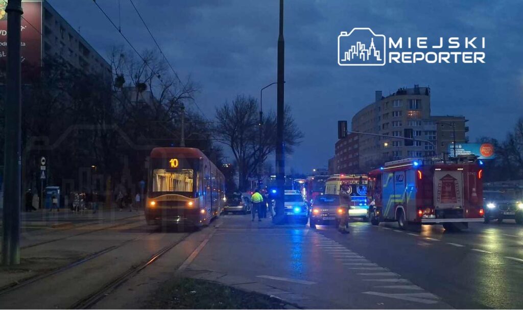 Tramwaj linii 10 zatrzymany na torach, obok pojazdy służb ratunkowych i policji w ciemnej scenerii wieczornej.