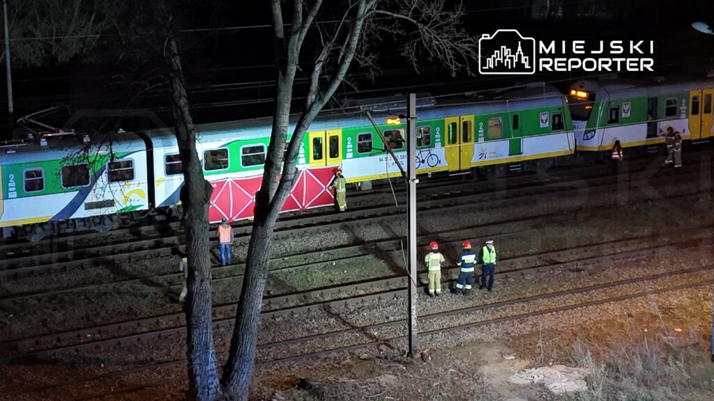Na torach kolejowych stoi pociąg z kolorowymi malunkami, a obok pracują strażacy i ratownicy w odblaskowych kamizelkach.
