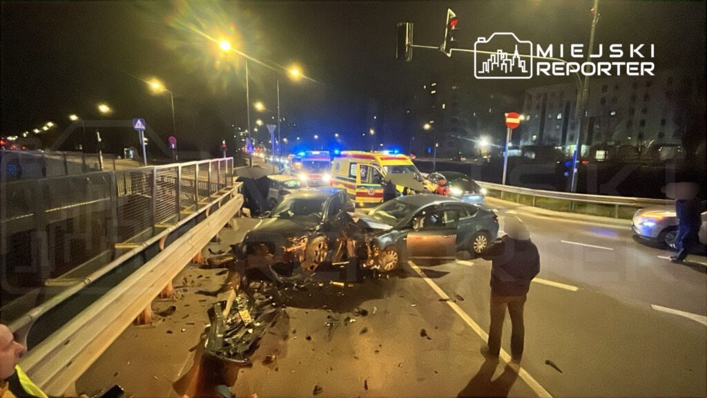 Dwa zderzone samochody na ruchliwej ulicy, w tle widać radiowozy i karetkę, a przy nich kilka osób.