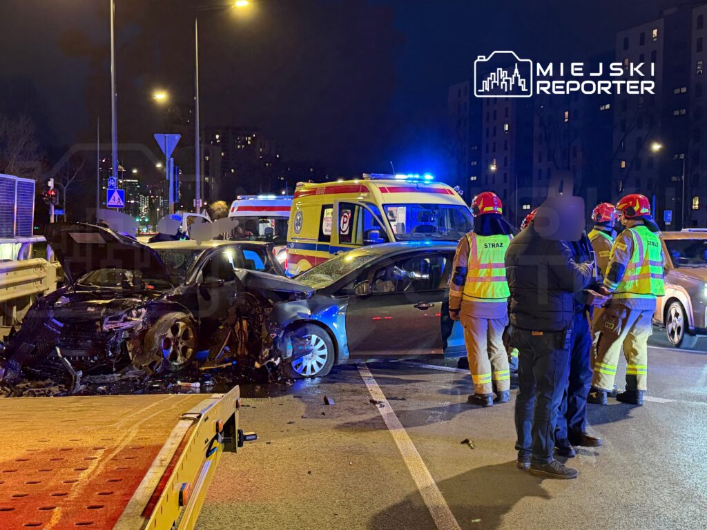 W nocy na ulicy doszło do wypadku samochodowego, w którym uczestniczyły dwa uszkodzone pojazdy. Obecni strażacy oraz karetka udzielają pomocy.