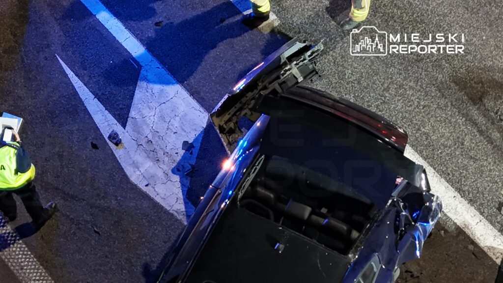 Policyjny funkcjonariusz notujący szczegóły wypadku drogowego na uszkodzonym pojeździe w nocy.