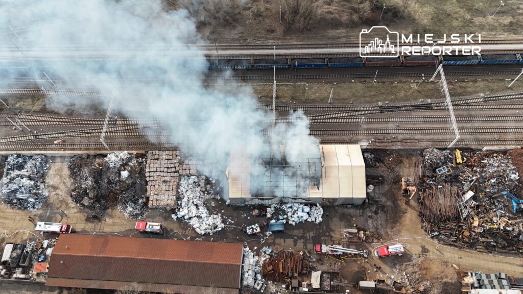 Dym unoszący się z płonącego magazynu na terenie zakładu recyklingowego, w pobliżu torów kolejowych.