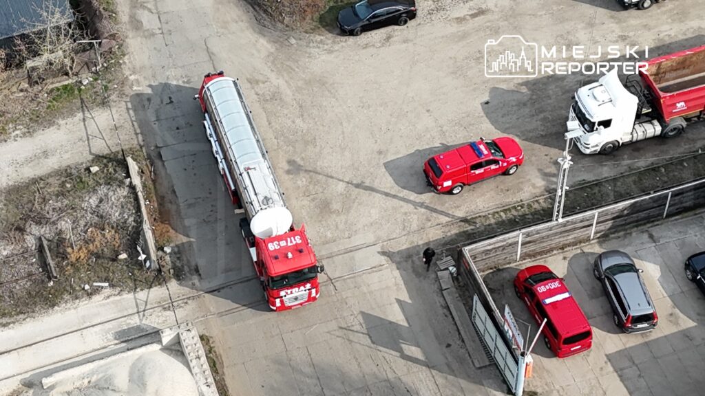 Czerwony wóz strażacki i policyjny parkowane na wyboistej drodze, obok ciężarówki z ładunkiem.