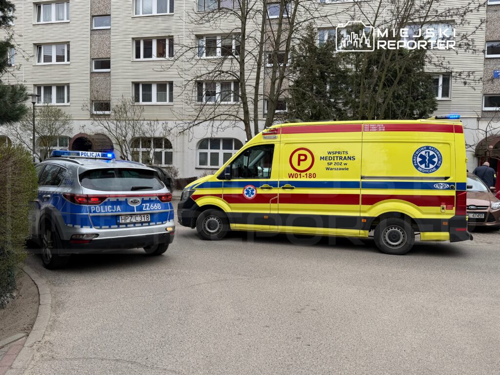 Radiowóz policyjny z włączonymi sygnałami świetlnymi stoi obok karetki pogotowia w pobliżu budynku mieszkalnego.