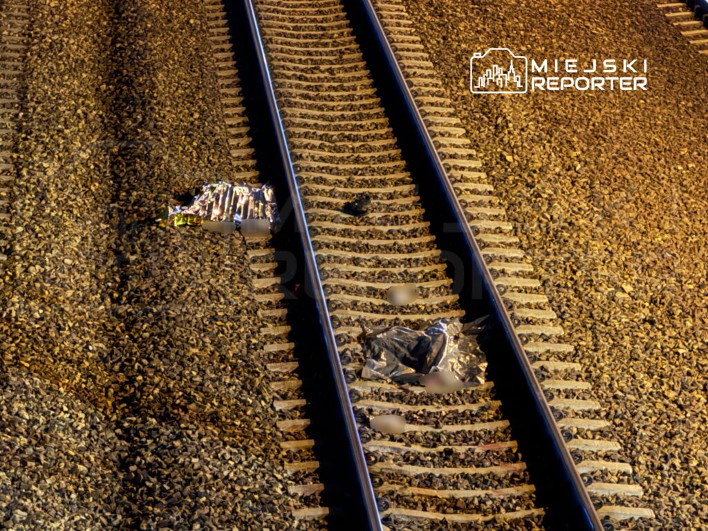 Na torach kolejowych leżą dwa przedmioty w folii oraz materiał, otoczone żwirkiem.