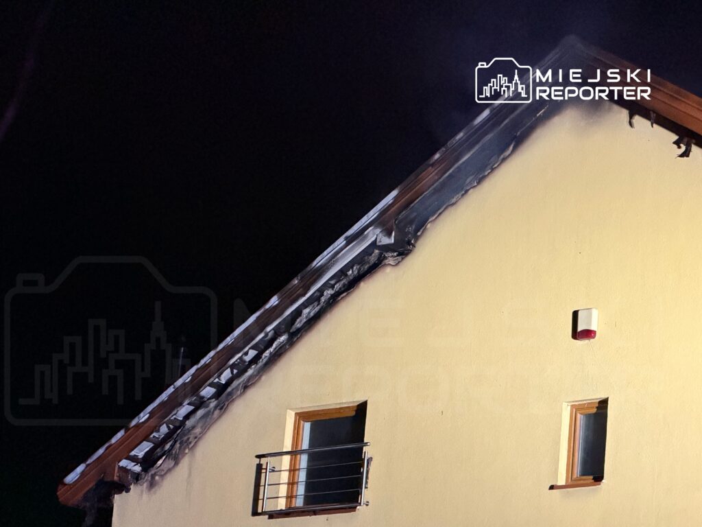 Uszkodzona elewacja domu z wypaloną częścią dachu, z widocznymi śladami po pożarze.