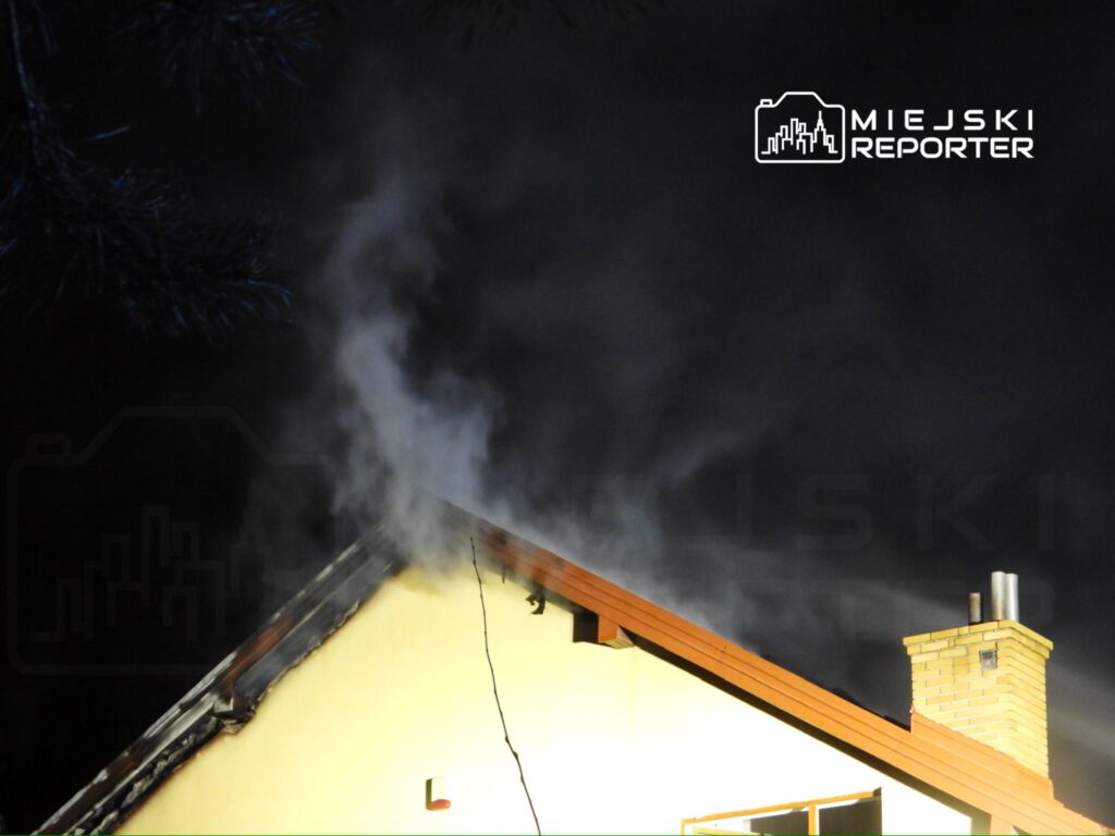 Z komina budynku wydobywa się dym w ciemnej scenerii nocnej.