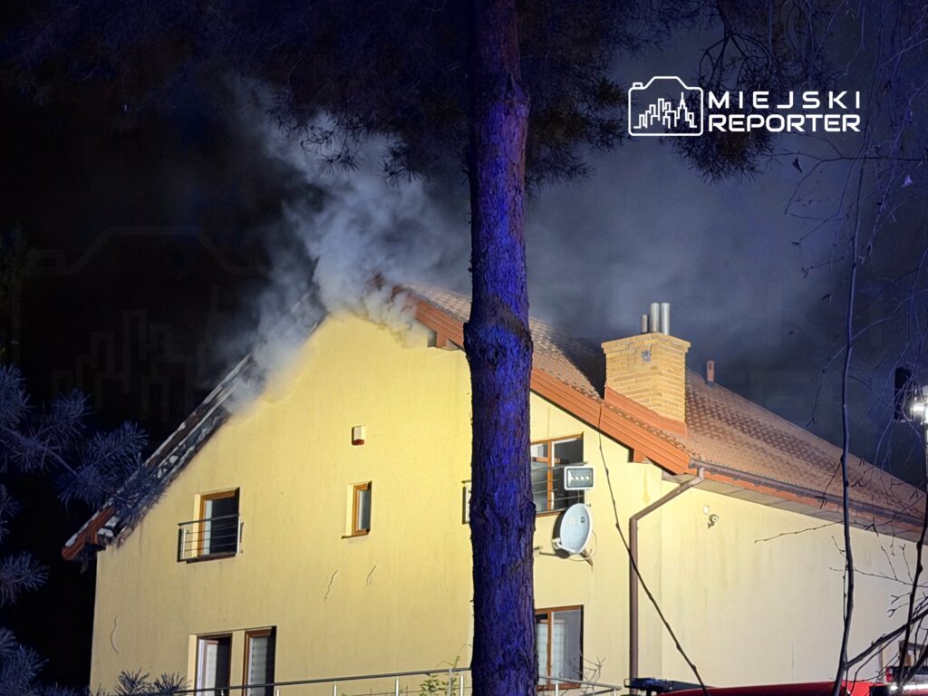 Dym wydobywający się z dachu nowoczesnego domu jednorodzinnego otoczonego drzewami w nocy.