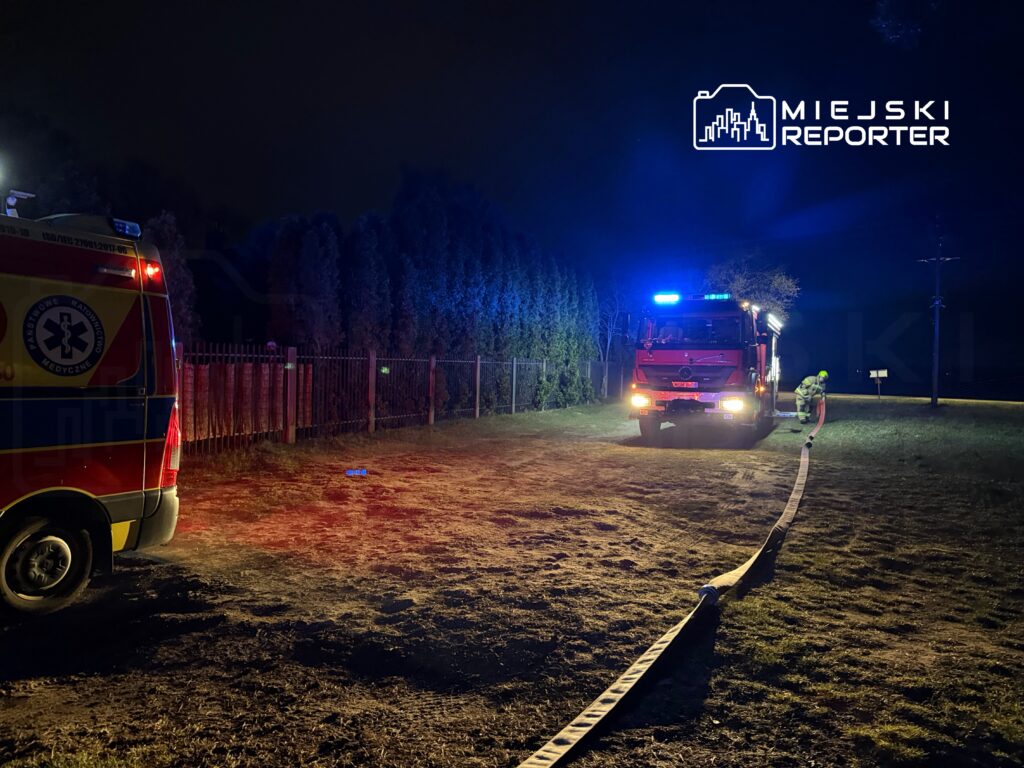 Zespół ratownictwa medycznego i straż pożarna pracują na nocnej akcji w terenie, rozkładając węże.