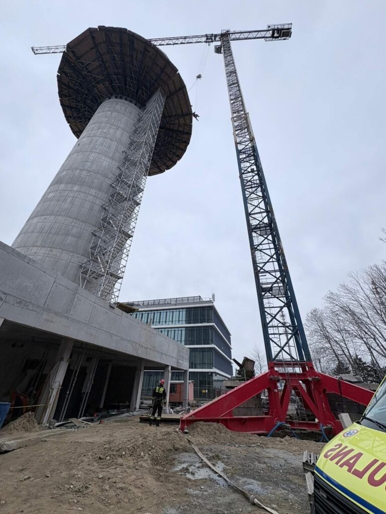 Robotnik w kasku obserwujący budowę nowoczesnego wieżowca z dźwigiem i betonową konstrukcją w tle.