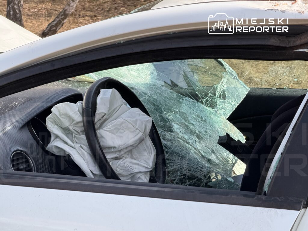 Wnętrze uszkodzonego samochodu z rozwiniętym poduszką powietrzną i rozbitym przednim szyby.
