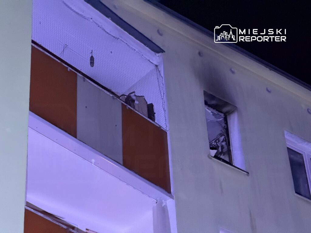 Uszkodzona elewacja budynku z widocznymi śladami po pożarze oraz oknem z zniszczonymi ramami.