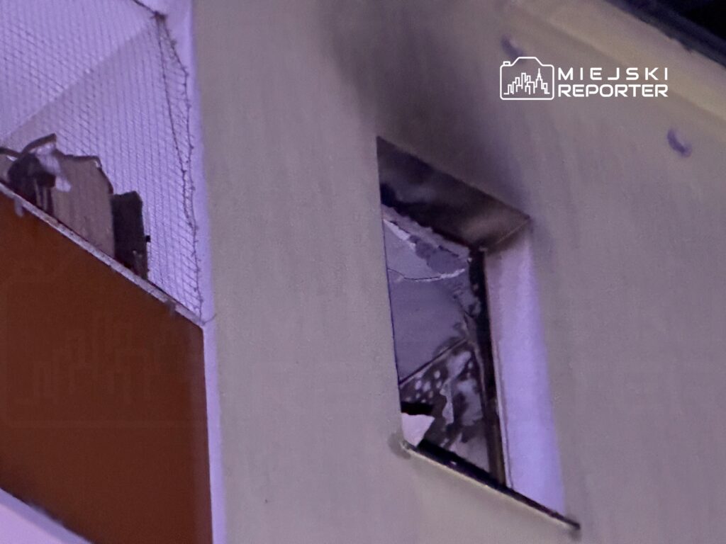 Zniszczone okno w budynku mieszkalnym, z widocznymi fragmentami uszkodzonej ramy i zasłon.