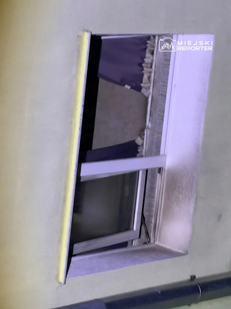 Okno z metalową ramą otwarte na zewnątrz, z zasłoną w kolorze fioletowym, w jasnym wnętrzu budynku.