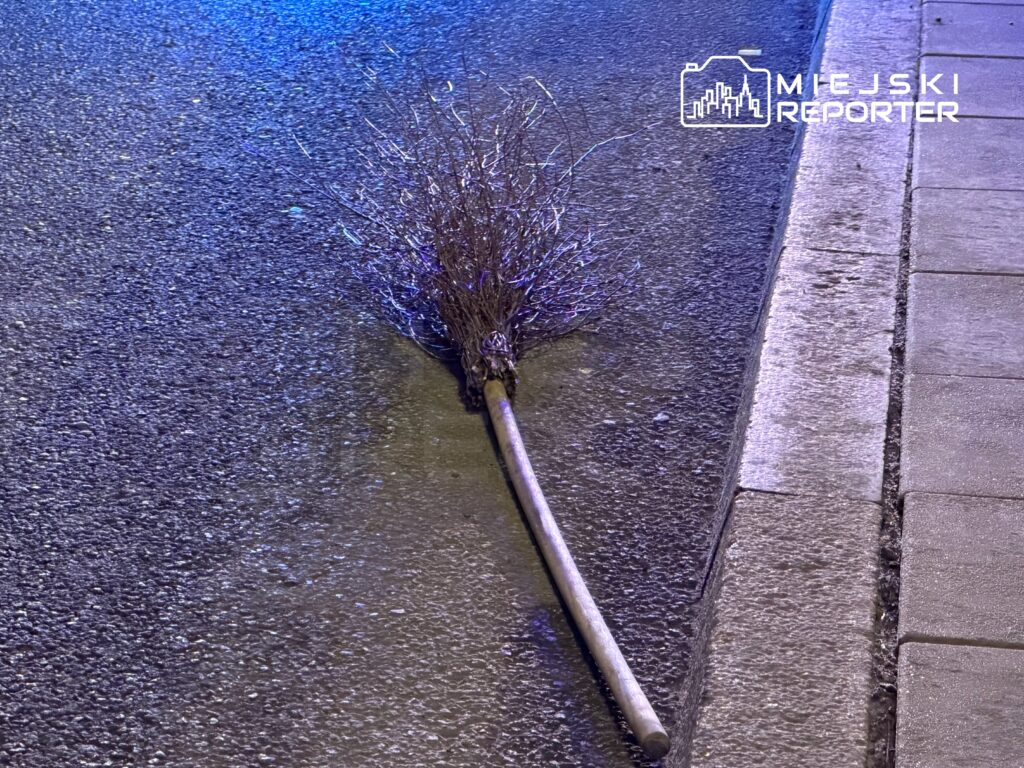 Miotła leżąca na ulicy, obok krawężnika, w oświetleniu nocnym.