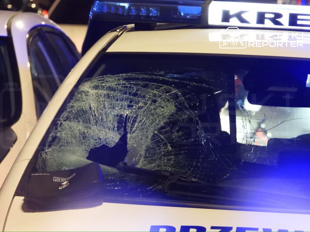 Rozbita szyba w radiowozie policyjnym z widocznymi pęknięciami, zaparkowanym w nocy.