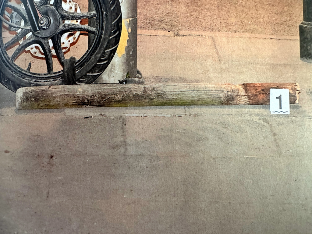 Na chodniku leży kawałek drewna oznaczony numerem 1, obok znajduje się tylna część roweru.