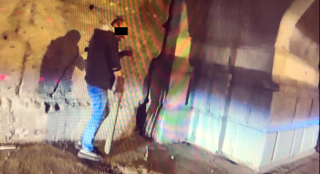 Mężczyzna w ciemnej bluzie używa narzędzia do pracy w opuszczonym pomieszczeniu z betonowymi ścianami.