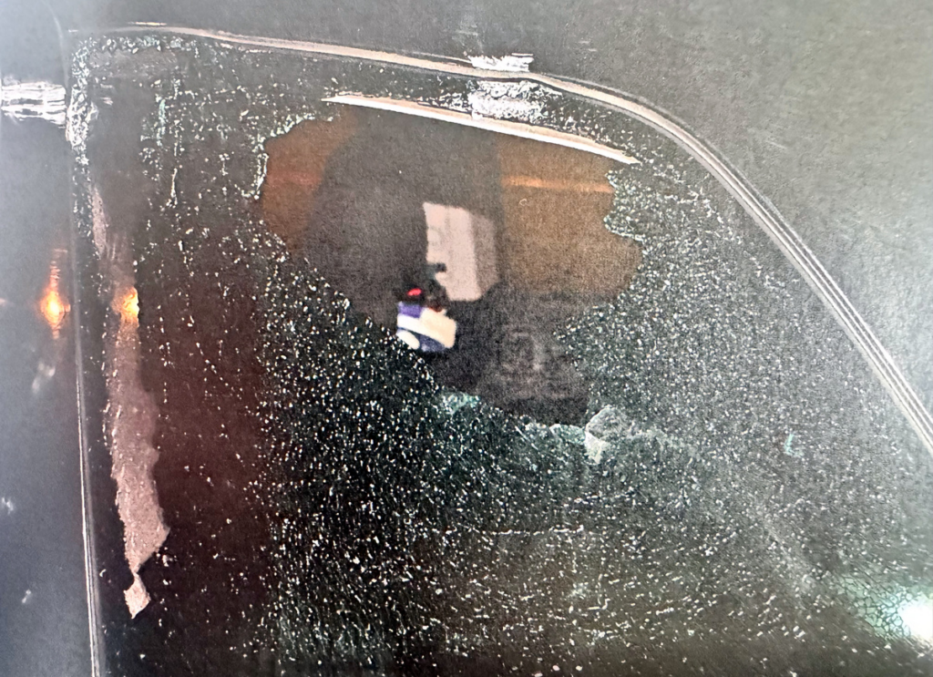 Pęknięte okno samochodu z widocznymi fragmentami szkła i odbiciem zewnętrznego otoczenia.