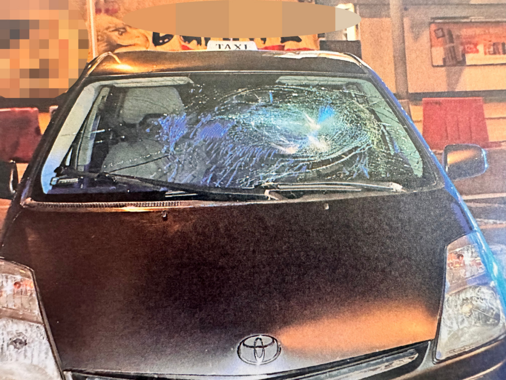 Uszkodzony samochód osobowy z rozbitą przednią szybą, stojący na oświetlonej ulicy.