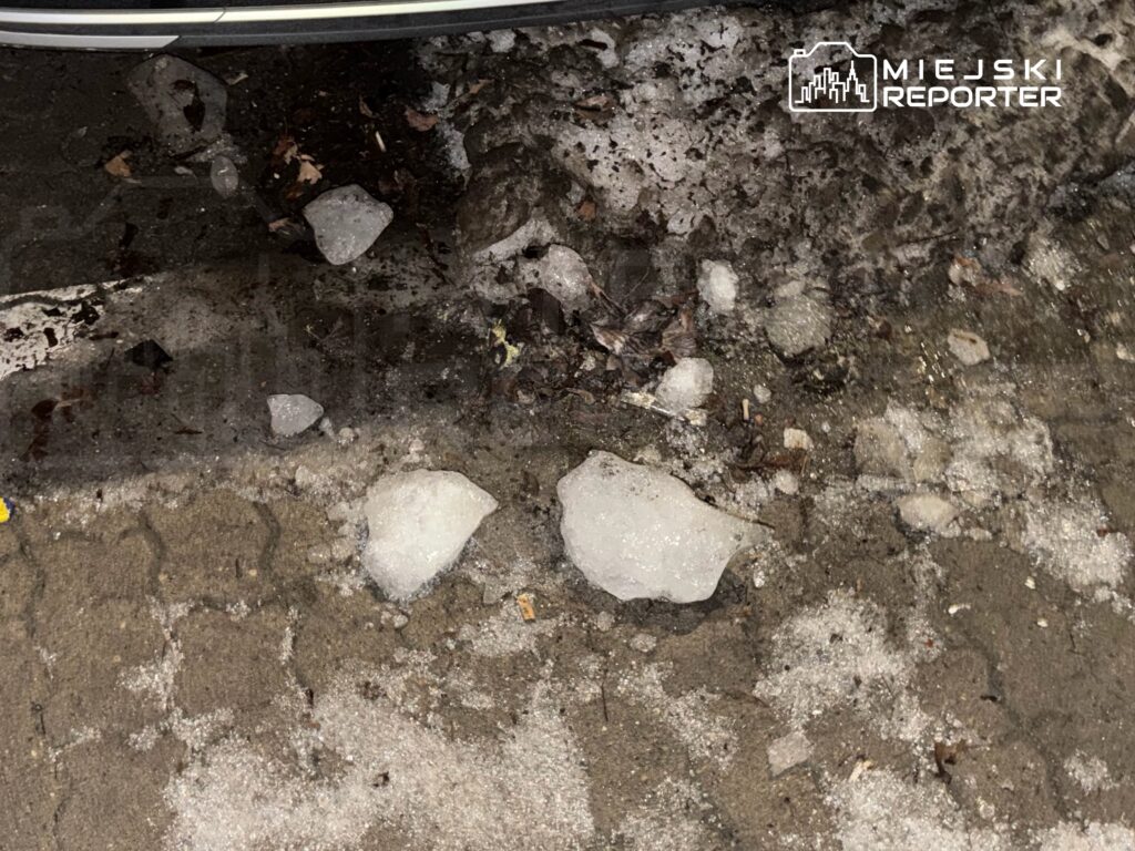 Na chodniku leżą kawałki lodu oraz błoto, w otoczeniu widoczne ślady po topniejącym śniegu.