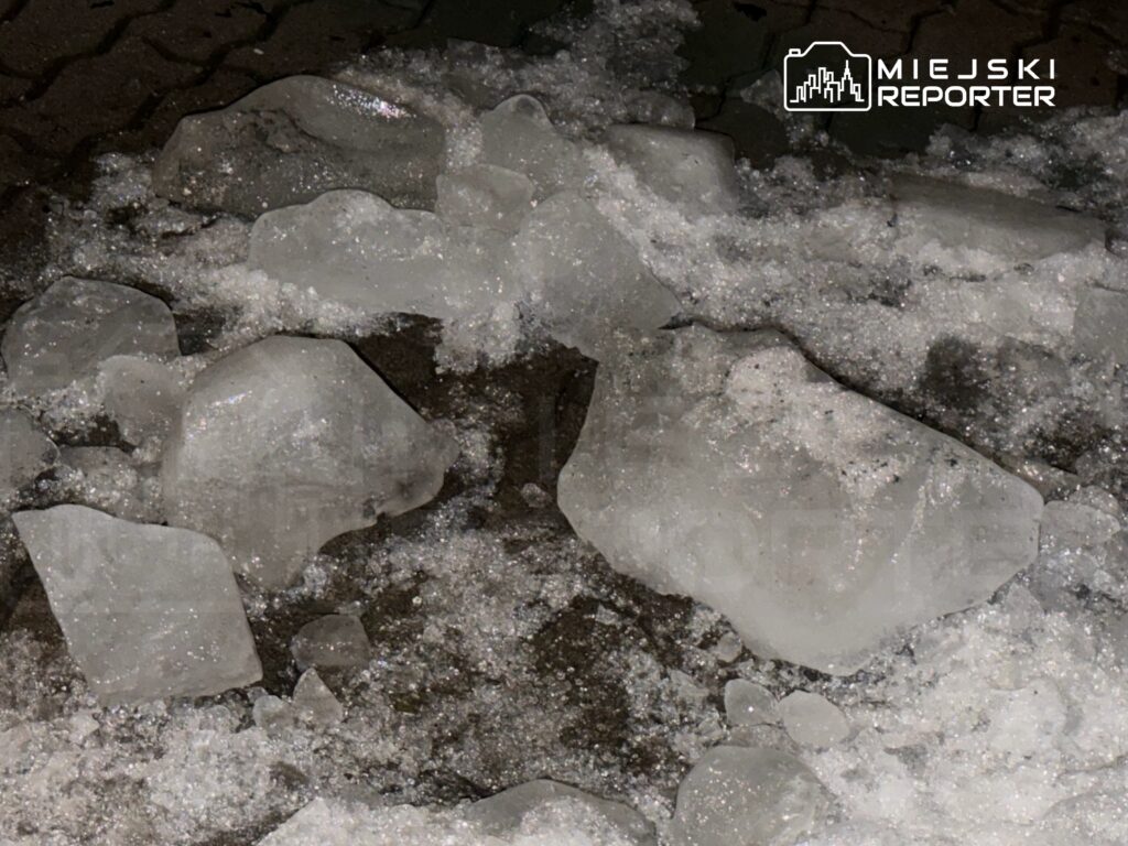 Skruszone kawałki lodu leżą na mokrej nawierzchni, otoczone drobnym śniegiem.