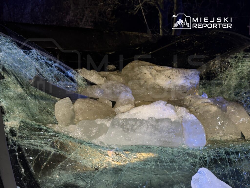 Szkło samochodu pokryte dużymi bryłami lodu, w nocy, w otoczeniu ciemnego tła z drzewami.