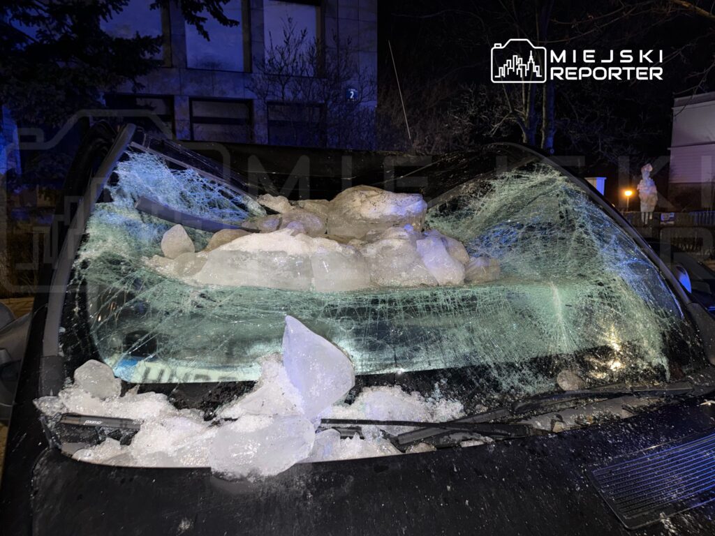 Szyba przednia samochodu pokryta dużymi kawałkami lodu i odłamkami szkła, w nocnym oświetleniu.