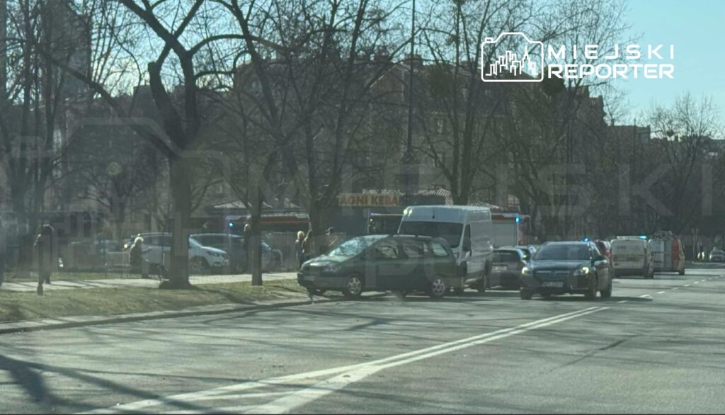 Zdarzenie drogowe z udziałem dwóch pojazdów na ulicy, otoczone przez służby ratunkowe oraz przechodniów.