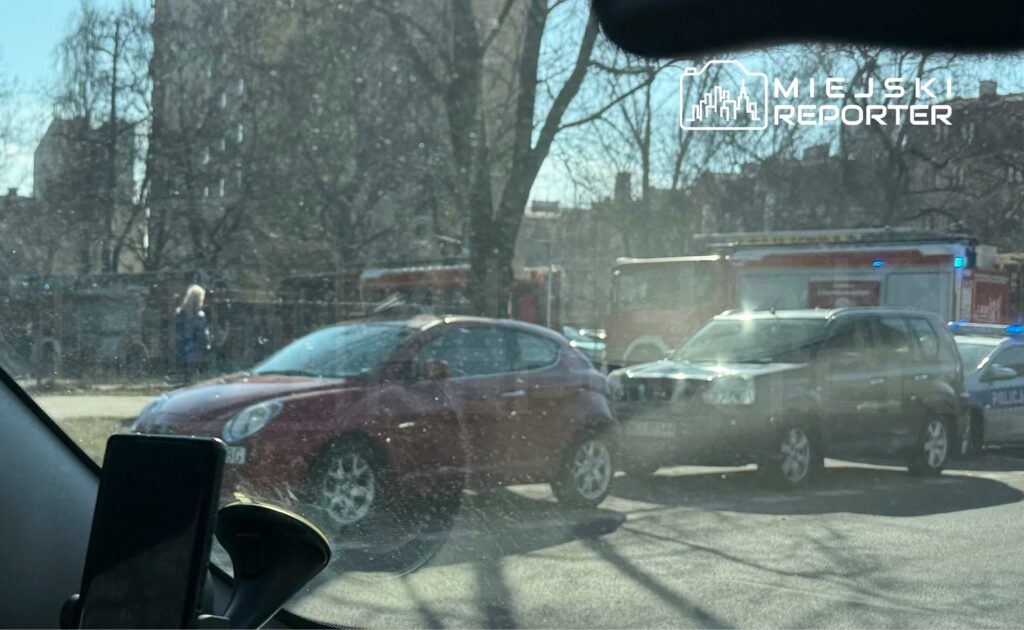 Czerwony samochód osobowy zatrzymany obok radiowozu policyjnego, w tle widać woz strażacki.