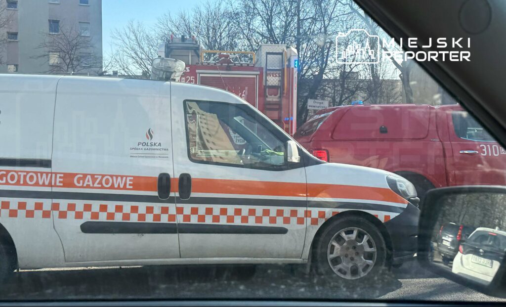 Samochód dostawczy z napisem "GOTOWIE GAZOWE" stoi w zatorze drogowym obok wozu strażackiego. W tle widoczne drzewa i budynki.