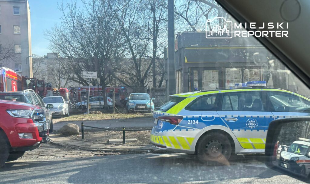 Na skrzyżowaniu ulic parkują radiowozy policyjne oraz samochody straży pożarnej, w tle widoczny budynek.