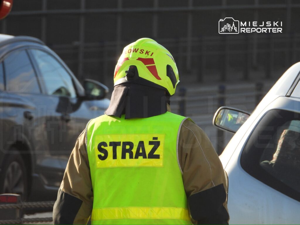 Strażak w kamizelce odblaskowej obserwujący ruch drogowy na miejskiej ulicy.