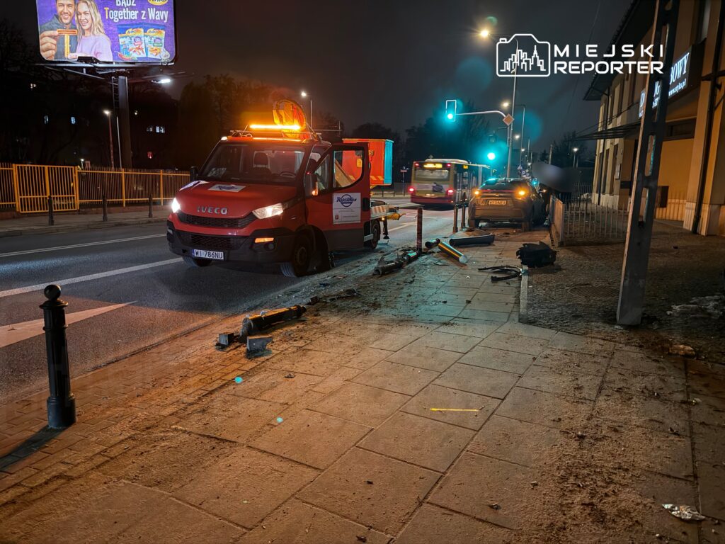 Czerwony samochód dostawczy z włączonymi światłami awaryjnymi stoi obok uszkodzonego pojazdu na oświetlonej ulicy.