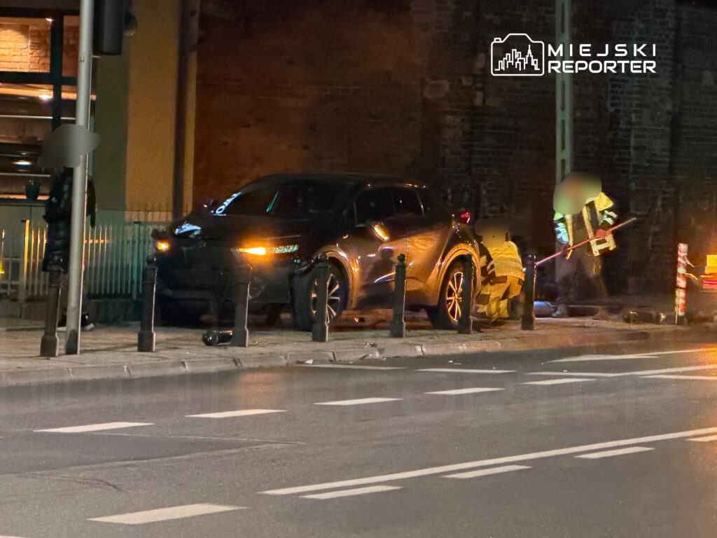 Grupa pracowników w kamizelkach odblaskowych przeprowadza prace naprawcze obok zaparkowanego samochodu na ulicy.