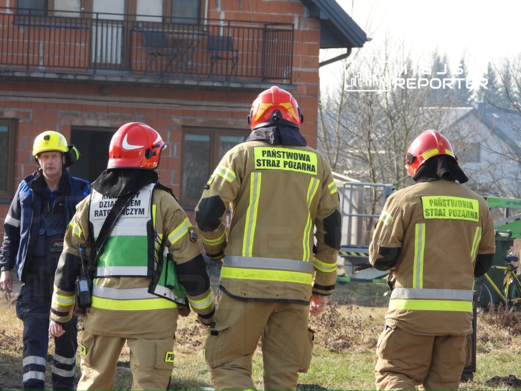 Grupa strażaków w mundurach ochronnych z logo "PAŃSTWOWA STRAŻ POŻARNA" ocenia sytuację na terenie budowy.