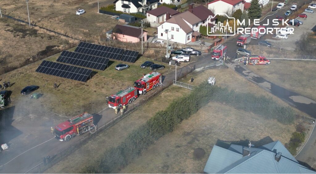 Strażacy pracują nad gaszeniem pożaru w pobliżu domów jednorodzinnych, obok paneli słonecznych.