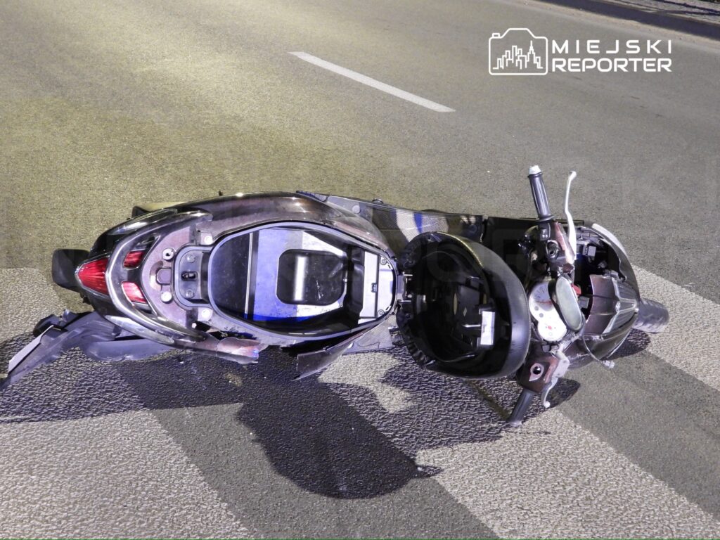 Rozbity skuter leżący na jezdni, z widocznymi uszkodzeniami nadwozia i częściami mechanicznymi.