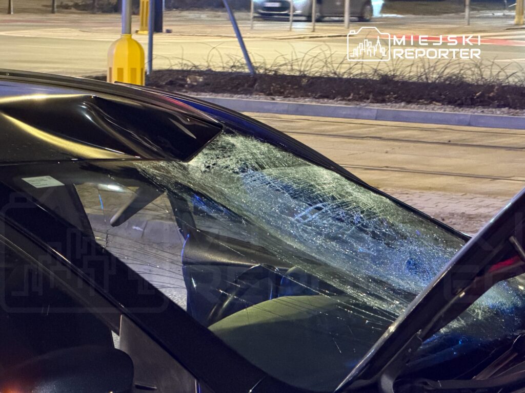 Uszkodzona szyba samochodu z widocznymi pęknięciami, zaparkowanego na oświetlonej ulicy.