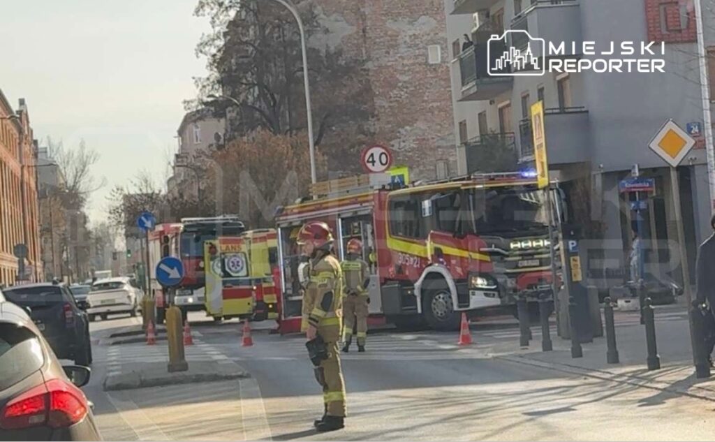 Strażak w mundurze stoi na ulicy obok wozów strażackich, blokując ruch w mieście.