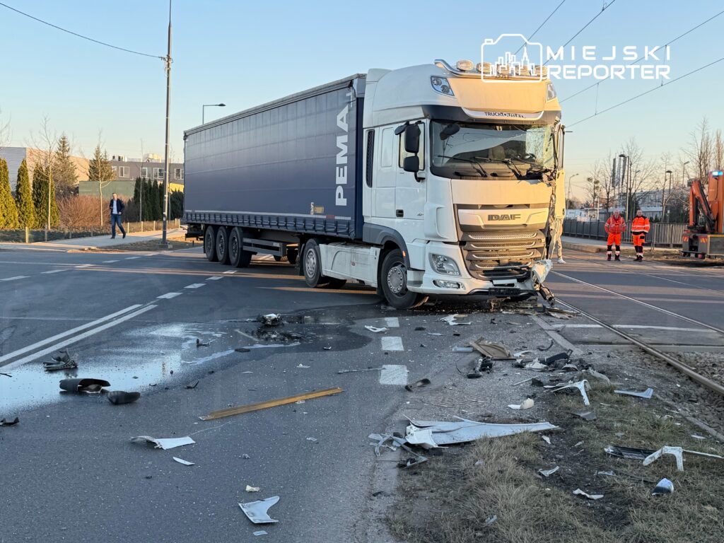 Ciężarówka z uszkodzoną przednią częścią stoi na skrzyżowaniu, a wokół rozrzucone są fragmenty pojazdu i plamy oleju.