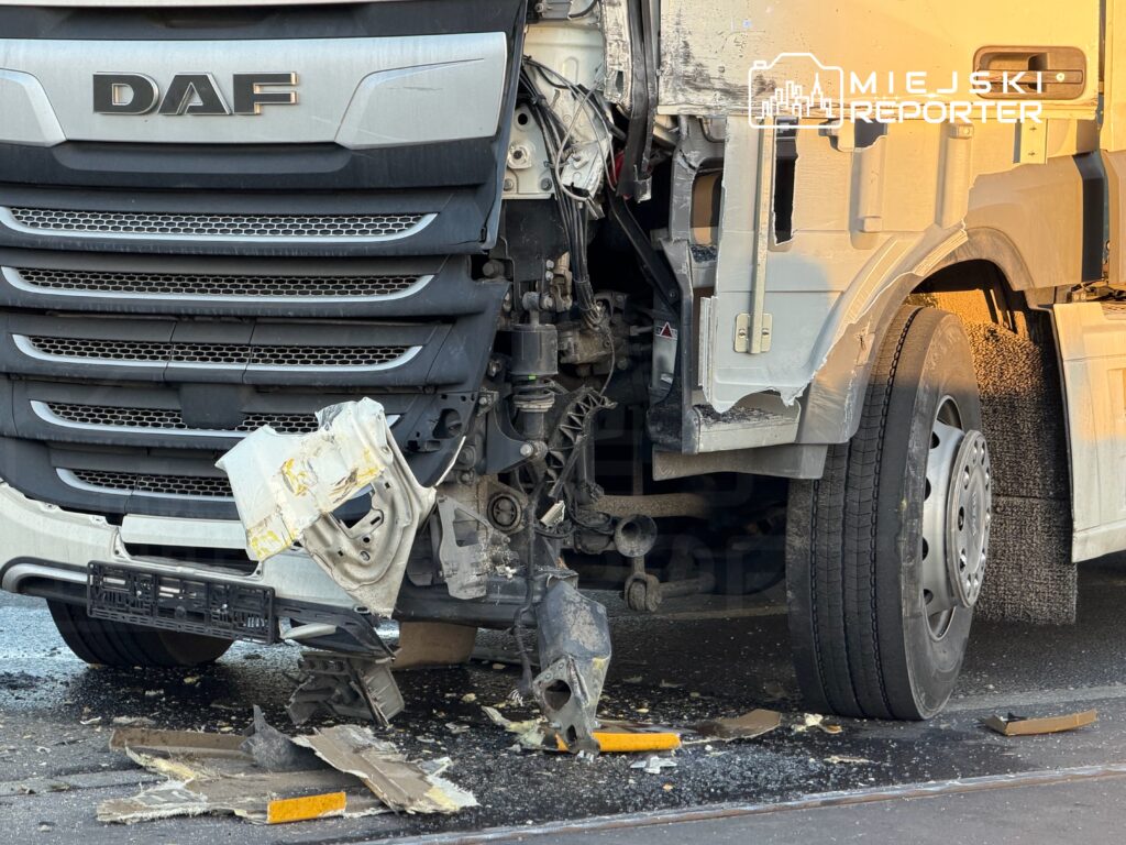 Uszkodzony przód ciężarówki DAF z oderwaną osłoną silnika, stojącej na jezdni w miejskim otoczeniu.