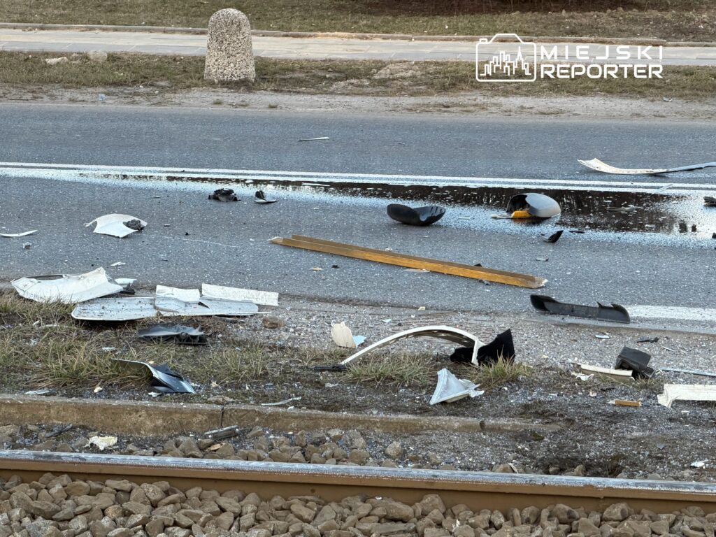 Na drodze leżą fragmenty zniszczonych elementów pojazdu, obok widoczna jest linia kolejowa.