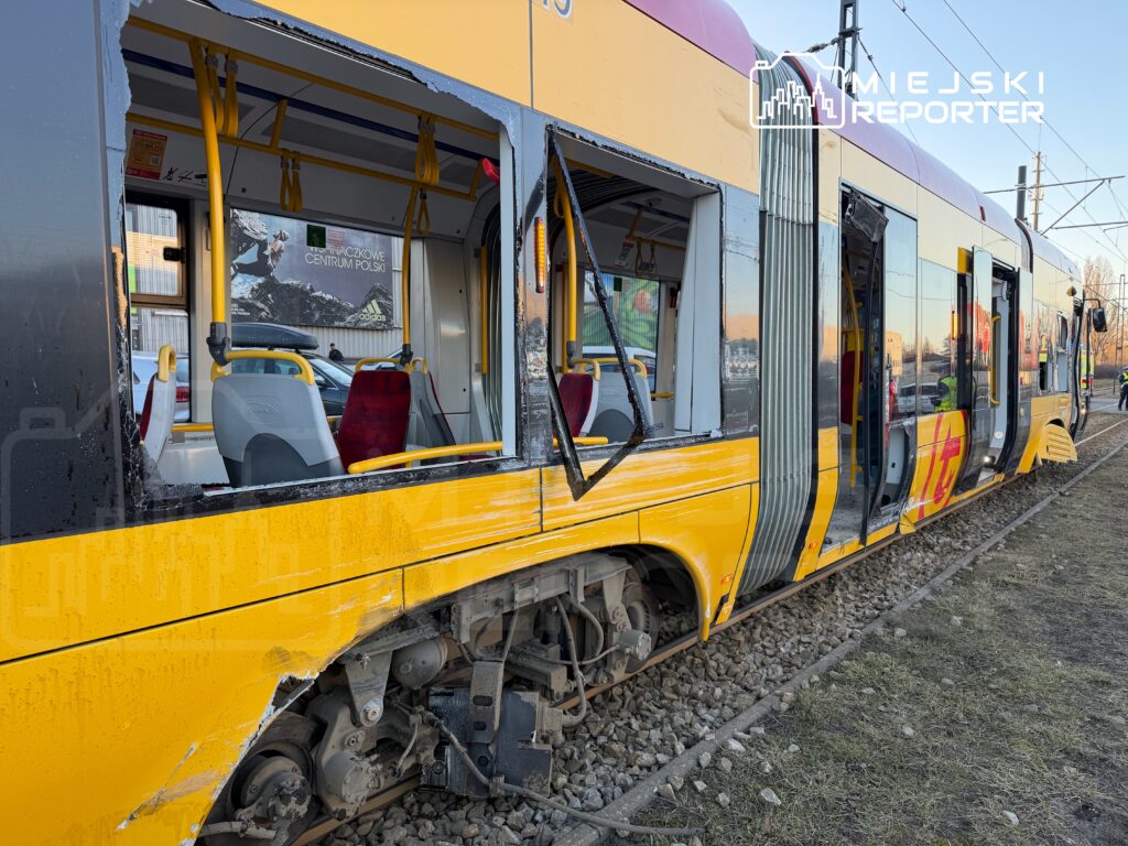 Zniszczony tramwaj z uszkodzoną boczną częścią stoi na torach, obok widać puste siedzenia i żółte uchwyty.