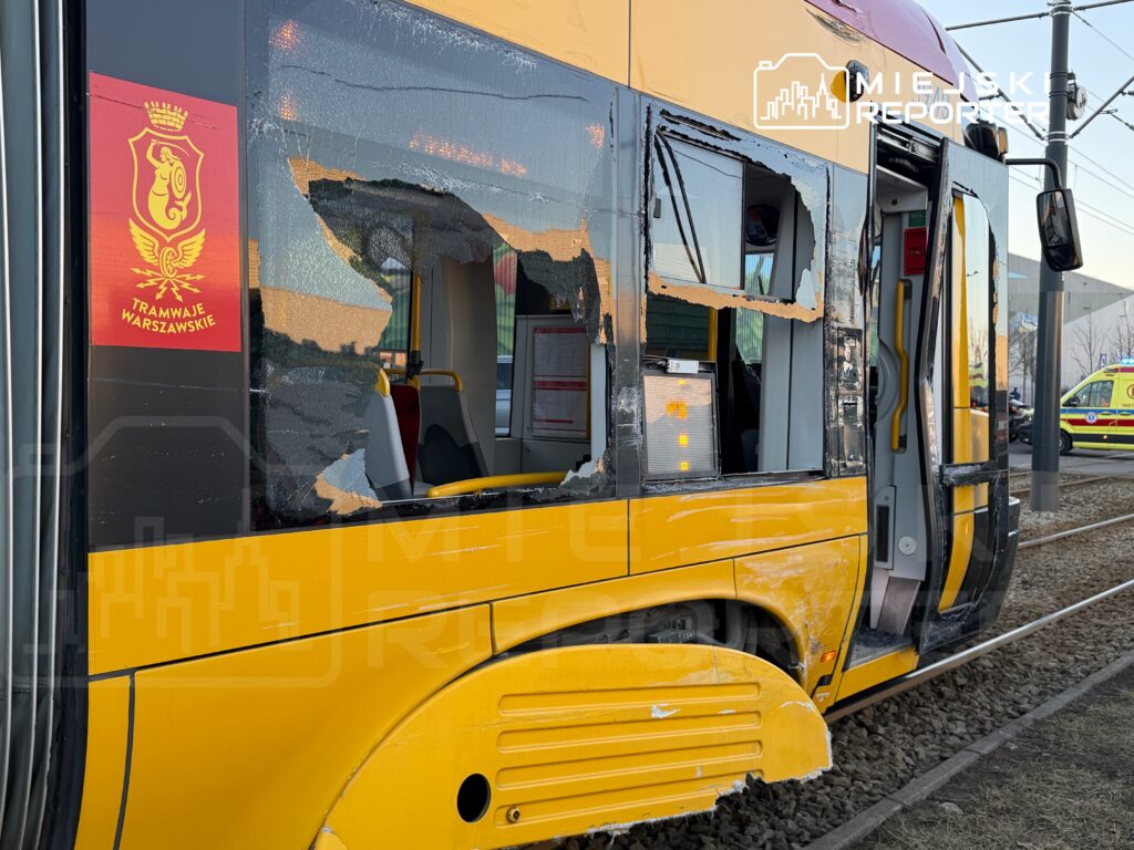 Uszkodzony tramwaj z dużym otworem w bocznej ścianie stoi na torach, obok widać służby ratunkowe.