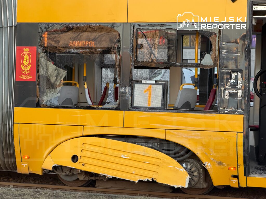 Zniszczony tramwaj z wybitymi szybami i uszkodzoną karoserią stoi na torach, z numerem linii wyświetlonym na tablicy.
