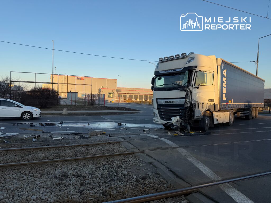 Wielka ciężarówka DAF z uszkodzoną przednią częścią stoi na skrzyżowaniu obok rozrzuconych szczątków. W tle widoczny budynek FedEx.