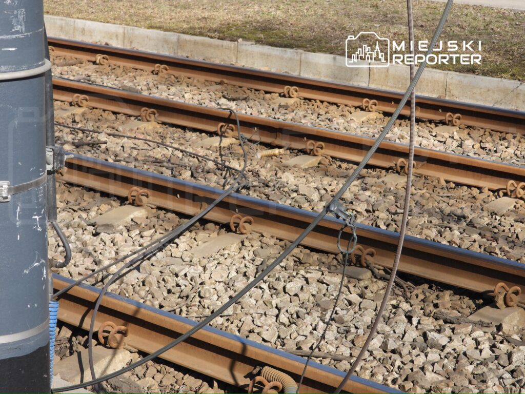 Elektrownia trakcyjna z przyłączonymi kablami nad torami kolejowymi na podłożu żwirowym.