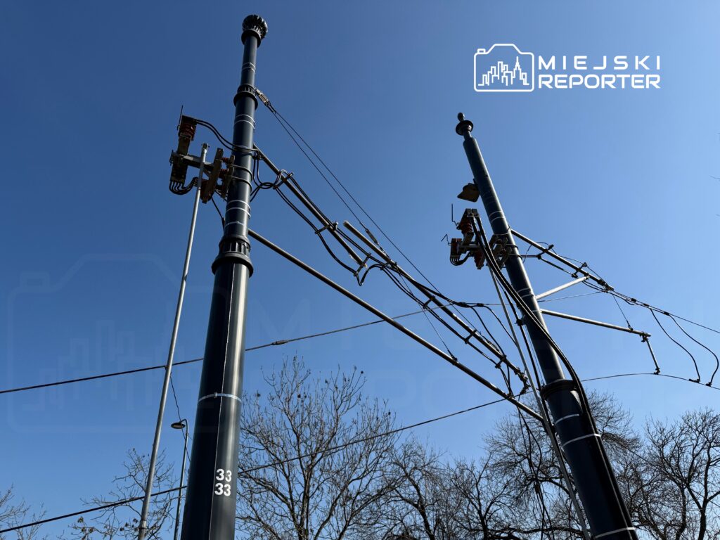 Wysokie słupy trakcyjne z rozciągniętymi przewodami na tle błękitnego nieba.