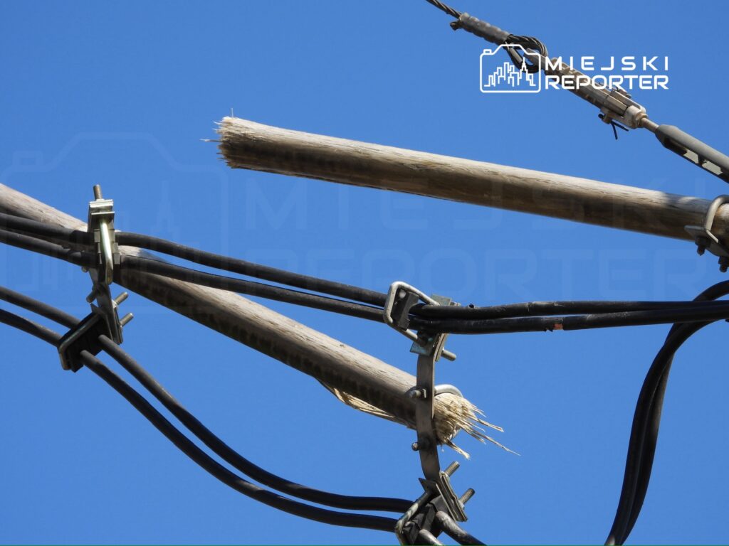 Uszkodzone przewody elektryczne zawieszone na słupie, na tle jasnoniebieskiego nieba.